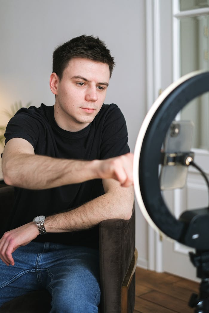 Adult male vlogger recording content using a phone and ring light indoors.